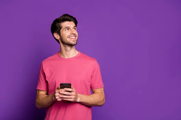 Portrait von positiven fröhlich süchtigen Kerl aussehen Kopie Raum verwenden Smartphone inspiriert denken, welche Art von Blog-Post Nachrichten tragen rosa Outfit isoliert über violetten hellen Glanz Farbe Hintergrund — Stockfoto