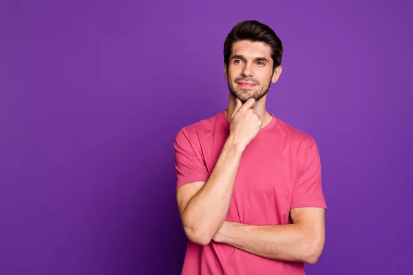 Φωτογραφία του ελκυστικού όμορφος άντρας καλή διάθεση χέρι στο πηγούνι ονειροπόλος εξετάσουμε ενδιαφέρον κενό χώρο έξυπνο δημιουργικό πρόσωπο φορούν casual ροζ t-shirt απομονωμένο πορφυρό φόντο χρώμα — Φωτογραφία Αρχείου