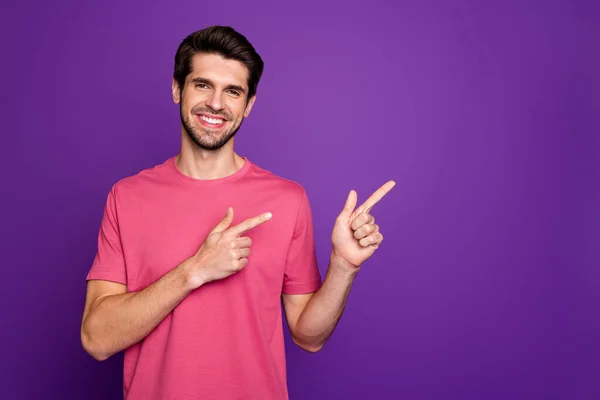 Foto van aantrekkelijke knappe man goed humeur directing vingers kant lege ruimte tonen cool aanbod winkelprijs dragen casual roze t-shirt geïsoleerde paarse kleur achtergrond — Stockfoto