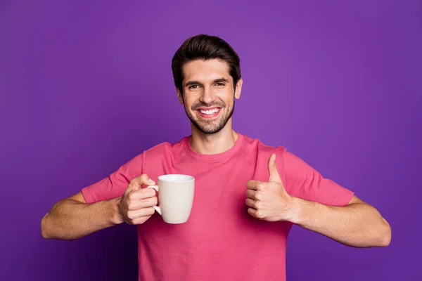 Foto de cara bonito atraente bom humor levantar polegar até o dente sorrindo segurar quente xícara de café desgaste casual rosa t-shirt isolado cor roxa fundo — Fotografia de Stock