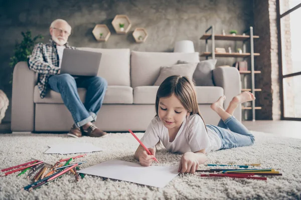 Zdjęcie dwóch osób dziadek pracuje online przeglądając laptop mała wnuczka leżąca podłoga dywan malarstwo kolorowe ołówki pobyt w domu kwarantanna salon w pomieszczeniach — Zdjęcie stockowe