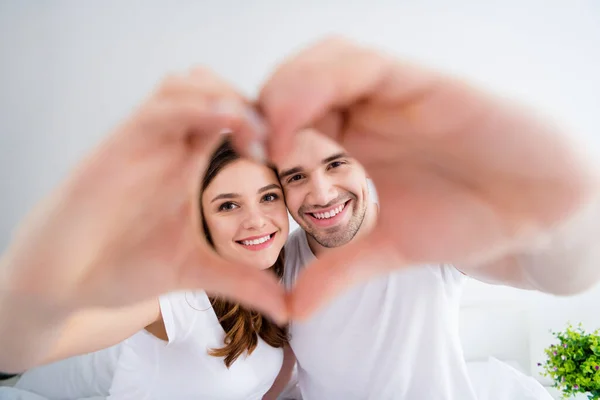 Primeros planos enfoque borroso foto de adorable dama guapo chico casado pareja juntos se agarran de la mano haciendo figura del corazón gesto que simboliza los sentimientos cardíacos desgaste sala de pijama en el interior — Foto de Stock