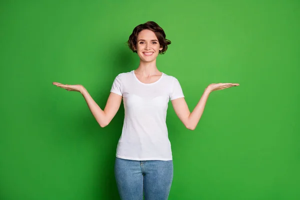 美丽的女士波浪型短发的照片张开双臂空旷的空间展示新奇的建议选一件最好的休闲服白色T恤牛仔裤孤立的绿色背景 — 图库照片