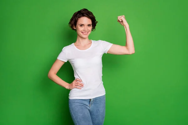 Photo of attractive self-sure lady faliste bobbed hairdo demonstrujące idealny kształt biceps ramię wygrać konkurs nosić casual biały t-shirt dżinsy odizolowane jasny zielony kolor tła — Zdjęcie stockowe