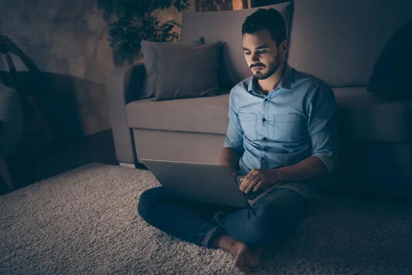 Retrato de su agradable chico morena enfocado atractivo sentado en el suelo trabajando remotamente exceso de trabajo el desarrollo de proyecto digital en el interior de estilo moderno sala de estar oscura oficina — Foto de Stock