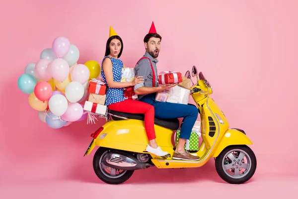 Pleine longueur profil côté photo étonné deux personnes motards conducteur tour scooter jaune transporter de nombreuses boîtes-cadeaux impressionné événement incroyable ont des boules d'air voler isolé fond de couleur rose — Photo