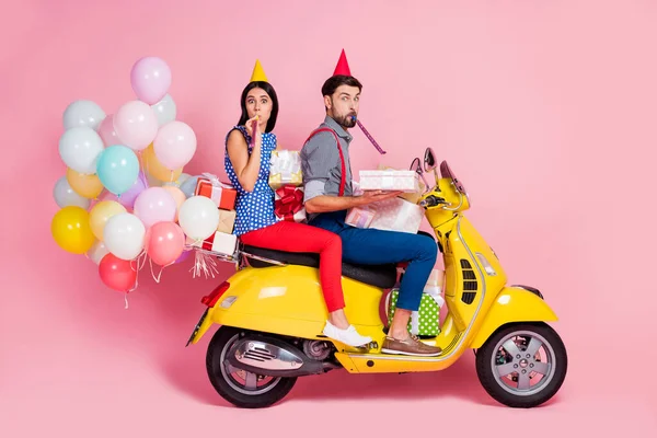 Full body profile side photo funny two people friends drive chopper deliver gift boxes whistle blower air baloons fly wear birthday cones shirt pants dotted retro red isolated pink color background — Stock Photo, Image