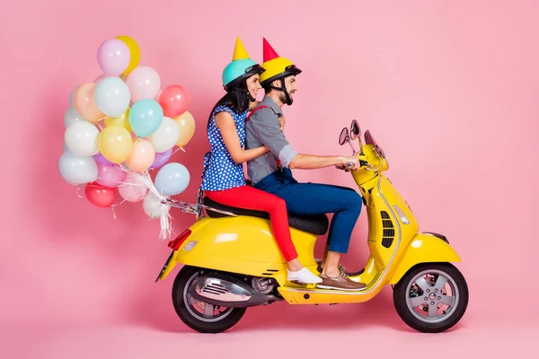 Full size profile side photo positive wife husband two people drive yellow choppers anniversary party have air baloons fly wear shirt pants red cone hat isolated pastel color background — стоковое фото