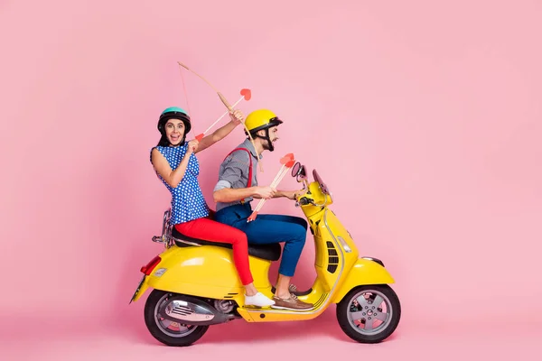 Full length profil strana photo crazy two people biker amour motorcyclist riders drive yello0w motor bike fast speed on 14-únor výlet shoot arrow red hearts isolated pink color background — Stock fotografie