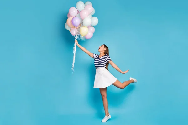 Full size φωτογραφία προφίλ της όμορφης funky κυρία κατέχουν πολλά πολύχρωμα μπαλόνια πετούν μέχρι άνεμος φυσάει φορούν ριγέ t-shirt λευκό κοντά υποδήματα φούστα απομονωμένο μπλε χρώμα φόντο — Φωτογραφία Αρχείου