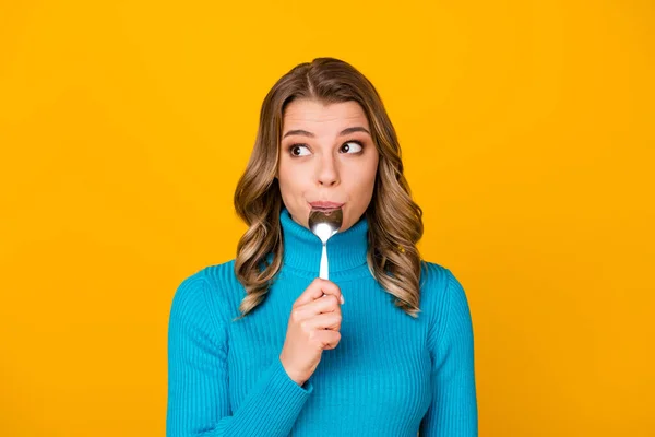 Foto de encantadora señora rizada divertida mantenga cuchara de metal en la boca mirada tentadora espacio vacío sueño de comida sabrosa cena desgaste cuello alto azul aislado brillo brillante color amarillo fondo — Foto de Stock