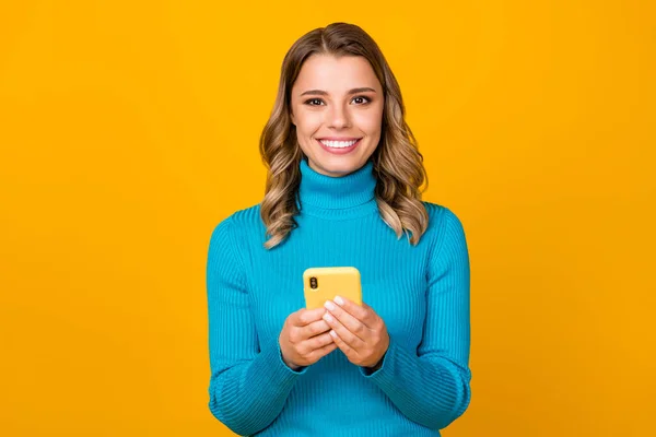 Foto der attraktiven lockigen Bloggerin gute Laune halten Telefonhände schreiben kreative Post tragen lässig blau warmen Rollkragen isoliert lebendigen gelben Farbhintergrund — Stockfoto