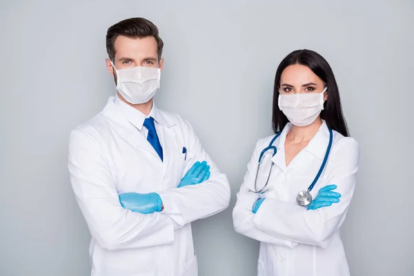 Foto de dos especialistas doc guy lady virología clínica médicos experimentados brazos doblados desgaste protector antigripal máscaras faciales guantes batas de laboratorio aislado fondo de color gris — Foto de Stock