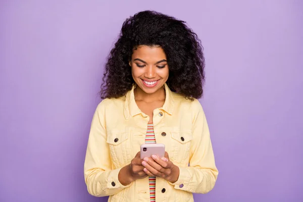Portrét pozitivní veselý afro americká dívka pomocí svého smartphone čtení sociální sítě zpravodajství chatování s přáteli nosit ležérní oblečení izolované fialové barvy pozadí — Stock fotografie