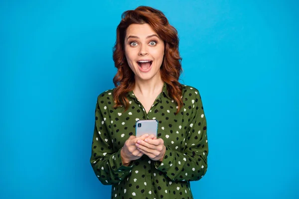 Foto di stupefacente bella signora tenere le mani del telefono aperto bocca controllare blog seguaci buone notizie ripubblicare commenti indossare verde punteggiato camicia isolato colore blu sfondo — Foto Stock