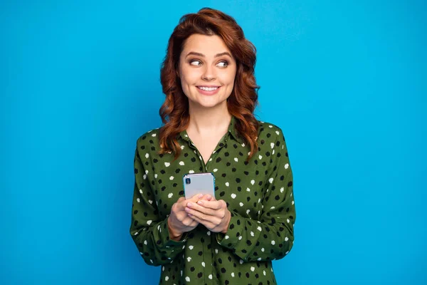 Foto de atraente engraçado senhora segurar telefone mãos viciado usuário olhar interessado lado vazio espaço complicado pessoa desgaste verde pontilhado camisa isolado azul cor fundo — Fotografia de Stock