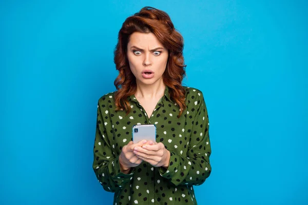 Foto van aantrekkelijke vrij gekke dame telefoon handen open mond check blog volgers lees negatieve reacties draag groen gestippelde shirt geïsoleerde blauwe kleur achtergrond — Stockfoto