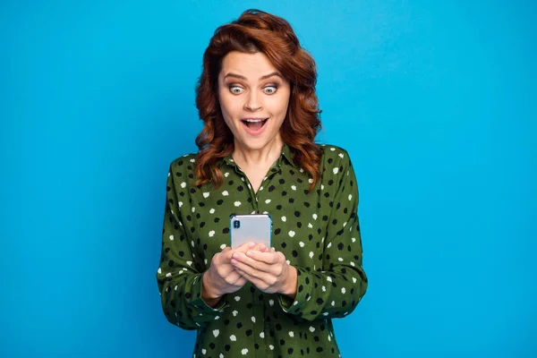 Photo of amazing pretty lady hold telephone hands open mouth check blog followers good news repost comments wear green dotted shirt isolated blue color background — Zdjęcie stockowe