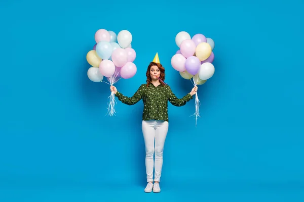 Ganzkörperfoto von ziemlich lustigen verrückten Dame halten zwei Arme viele bunte Luftballons Party Schlag Noisemaker tragen Geburtstagskappe gepunktetes Hemd weiße Hose Schuhe isoliert blaue Farbe Hintergrund — Stockfoto