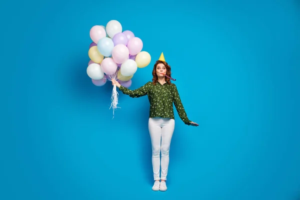 Полноразмерная фотография симпатичной смешной леди держать много цветных воздушных шаров лучший день рождения удар noisemaker носить день рождения фуражка пунктирная рубашка белые брюки туфли изолированный синий цветной фон — стоковое фото