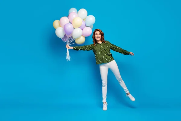 Foto de tamaño completo de la señora loca divertida llevar muchos globos de aire de colores fiesta de cumpleaños volando con el viento desgaste punteado camisa verde pantalones blancos zapatos aislados de color azul de fondo —  Fotos de Stock