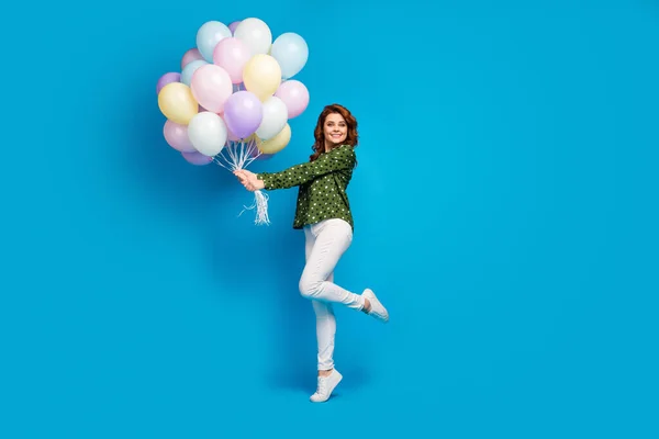 Πλήρης φωτογραφία προφίλ του σώματος του αστείο όμορφη κυρία κατέχουν πολλά πολύχρωμα μπαλόνια αέρα επισκεφθείτε πάρτι γενεθλίων φορούν διάστικτη πράσινο πουκάμισο λευκό παντελόνι παπούτσια απομονωμένο μπλε χρώμα φόντο — Φωτογραφία Αρχείου