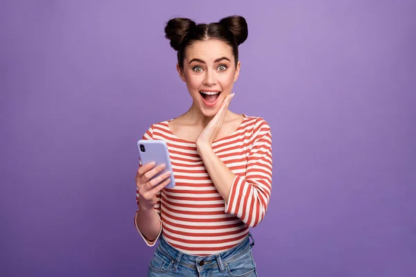Photo of funny lady two buns hold telephone check followers blog open mouth hand on cheek wear white red casual striped shirt isolated purple pastel color background — Stock Photo, Image