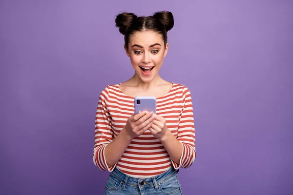 Photo of pretty lady two funny buns hold telephone hands check followers blog open mouth good news wear white red casual striped shirt isolated purple pastel color background