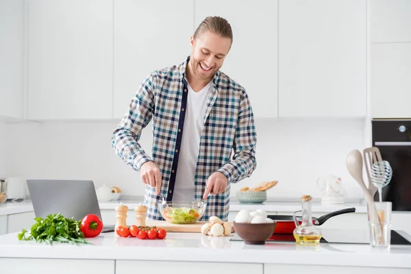 Портрет його привабливого веселого веселого хлопця, який робить смачний веганський обід з вітаміну, переглядає уроки відео-блогів у сучасному світло-білому інтер'єрі кухні в приміщенні — стокове фото