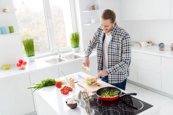 Foto de chico gourmet alegre positivo quiere cocinar sabrosa ensalada deliciosa para su esposa verter el desgaste de aceite casual camisa a cuadros en la casa de la cocina en el interior — Foto de Stock