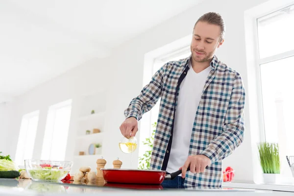 Foto de hombre guapo positivo cocinar sabrosa comida deliciosa cena verter aceite de girasol en la sartén usar casualmente a cuadros camisa de pie en la casa de la cocina — Foto de Stock