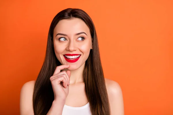 Primo piano foto di attraente allegra signora buon umore guarda interessato lato vuoto braccio spazio sul mento indossare casual canotta bianca isolato vibrante colore arancione sfondo — Foto Stock