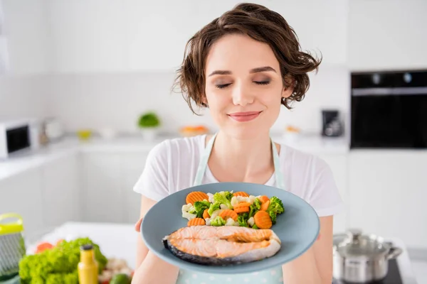 Close up photo of pretty housewife lady chef hold ready grilled salmon trout fillet steak with garnish cook dinner one person portion eyes closed wear apron t-shirt modern kitchen indoors — Stock Photo, Image