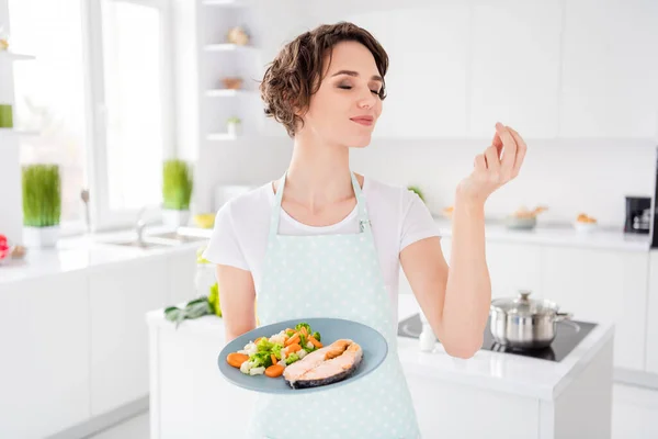 Foto de la señora bonita ama de casa chef mantenga listo salmón a la parrilla trucha filete asado condición con guarnición cocinar cena una persona porción usar delantal camiseta cocina moderna en el interior — Foto de Stock