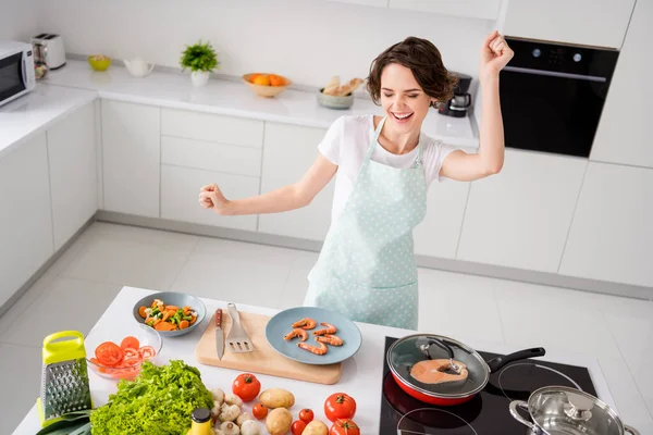 Foto de bela dona de casa alegre casca de senhora cozido camarões cozinhar e dançar animado preparados ingredientes saudáveis desgaste avental cozinha moderna dentro de casa — Fotografia de Stock