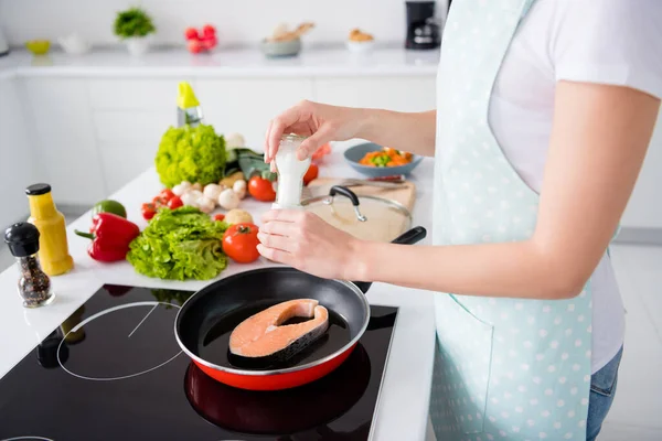 Beskuren bild av hemmafru dam händer sätta färsk rå lax filé stek liggande flygande pan lägga kryddor salt matlagning familj middag bära förkläde t-shirt stå modernt kök inomhus — Stockfoto