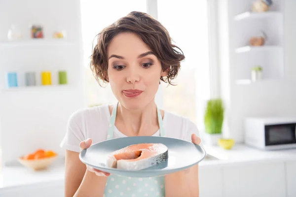 Close up photo of beautiful housewife lady enjoy look tempting fresh raw salmon fillet steak tasty diet breakfast tongue lick lips wear apron t-shirt stand modern kitchen indoors — Stock Photo, Image