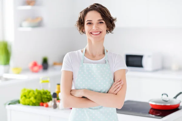 Foto de hermosa bobbed peinado ama de casa sosteniendo brazos cruzados disfrutar de la cocina de la mañana sabrosa cena familiar reunión desgaste delantal camiseta pie cocina moderna en el interior —  Fotos de Stock