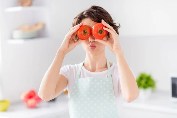 Foto von Hausfrau attraktive Dame Arme halten zwei große Tomaten verstecken Augen Senden Luftküsse verspielte Stimmung genießen morgens Kochen leckeres Abendessen tragen Schürze stehen moderne Küche drinnen — Stockfoto