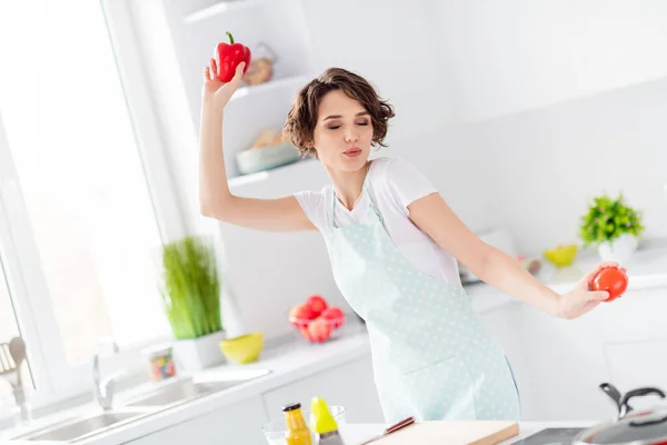 Φωτογραφία από το όμορφο αστείο σπίτι σύζυγος κρατήστε φρέσκο ντομάτα πιπέρι καμπάνα καλή διάθεση νόστιμο πρωινό χορό και μαγείρισσα ενθουσιασμένοι μάτια κλειστά ποδιά φθορά t-shirt σταθεί μοντέρνα κουζίνα σε εσωτερικούς χώρους — Φωτογραφία Αρχείου