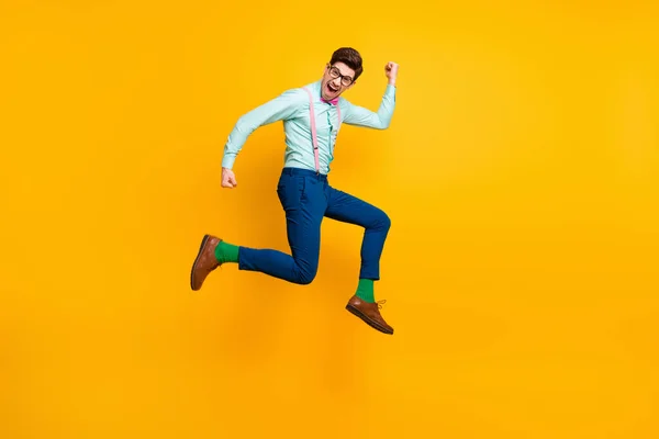 Full size profile photo of cool stylish guy jumping high up rejoicing winner wear specs shirt tie susenders trousers shoes green socks isolated bright yellow color background — стоковое фото