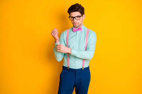 Photo of handsome cool clothes young guy boyfriend look empty space seriously buttoning shirt sleeve wear specs teal shirt pink suspenders bow tie trousers isolated yellow color background — Stock Photo, Image