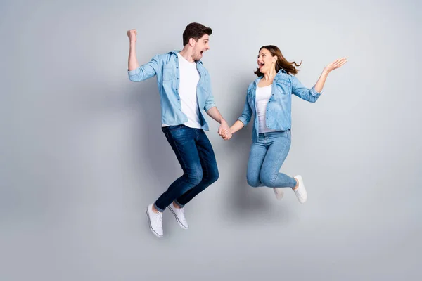 Фотографія повного розміру веселих двох студентів стрибок тримати руки святкувати вихідні лотереї знижка виграш носити повсякденні джинси ізольовані на сірому кольоровому фоні — стокове фото