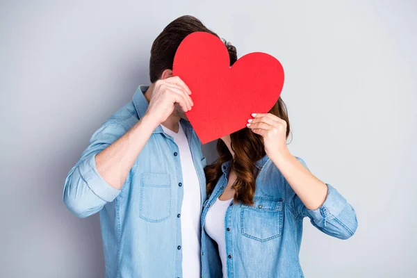 Portrait of tender gentle students couple man woman hide face with big red paper card heart kiss wear casual style jeans isolated over gray color background — Stock Photo, Image