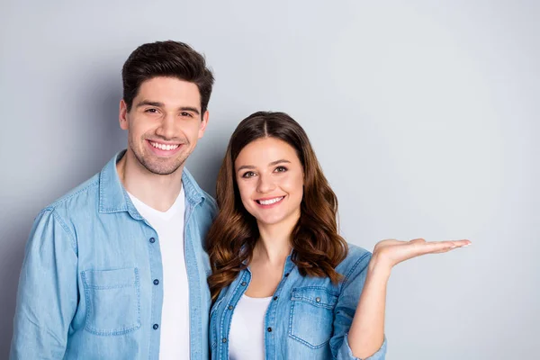 Foto atraente senhora bonito cara abraçando segurar braço aberto espaço vazio demonstrando novidade produto bom humor desgaste casual denim camisas isolado cinza cor fundo — Fotografia de Stock