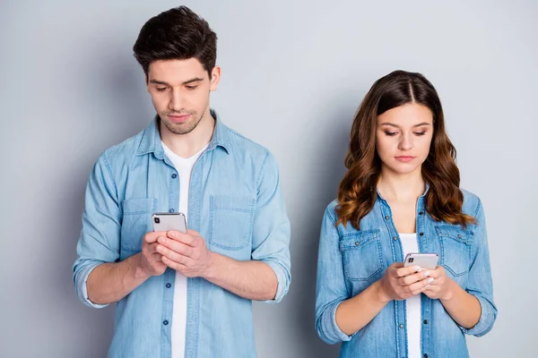 Foto mooie dame knappe man achteloos paar kijken telefoon scherm negeren elkaar verslaafde gebruikers dragen casual denim shirts outfit geïsoleerde grijze kleur achtergrond — Stockfoto