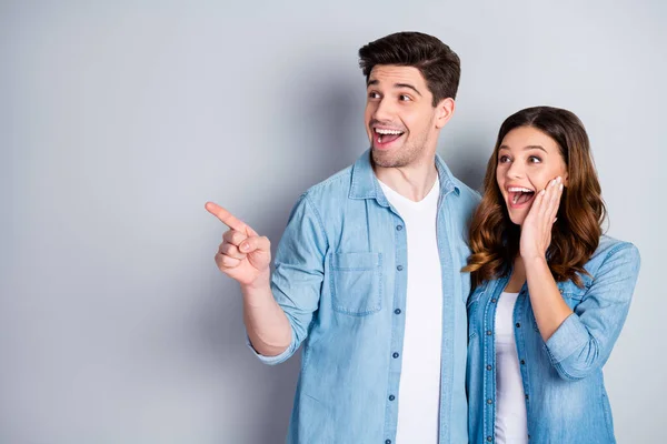 Photo two people funky lady crazy handsome guy direct finger empty space good news overjoyed hands on cheeks wear casual denim shirts outfit isolated grey color background — Zdjęcie stockowe