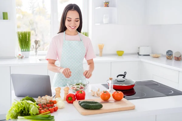 Foto van Aziatische etniciteit huisvrouw mengen verse groenten salade ingrediënten koken smakelijke veganistische maaltijd met behulp van online blogger recept notebook op tafel stand keuken binnen — Stockfoto