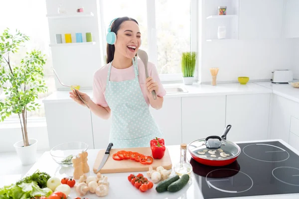 Портрет її вона приваблива весела весела дівчина робить свіжий домашній обід закуски гриби на сковороді електрична плита співаюча пісня хіт в сучасному світло-білому інтер'єрі кухні — стокове фото