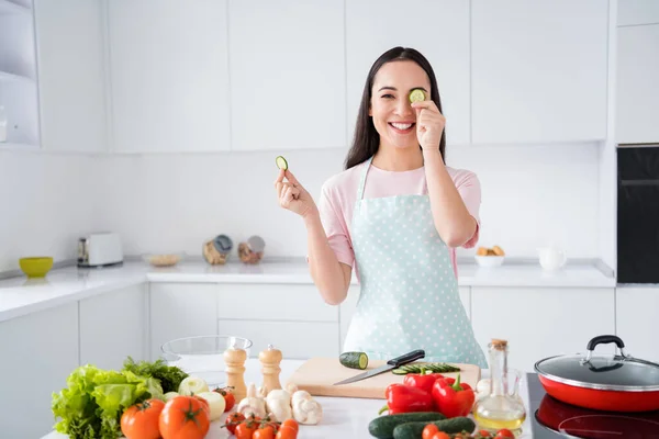 Foto van mooie aziatische etniciteit huisvrouw houden twee verse komkommer plakjes verbergen een oog speels stemming weekend koken lekker ontbijt salade stand keuken binnen — Stockfoto